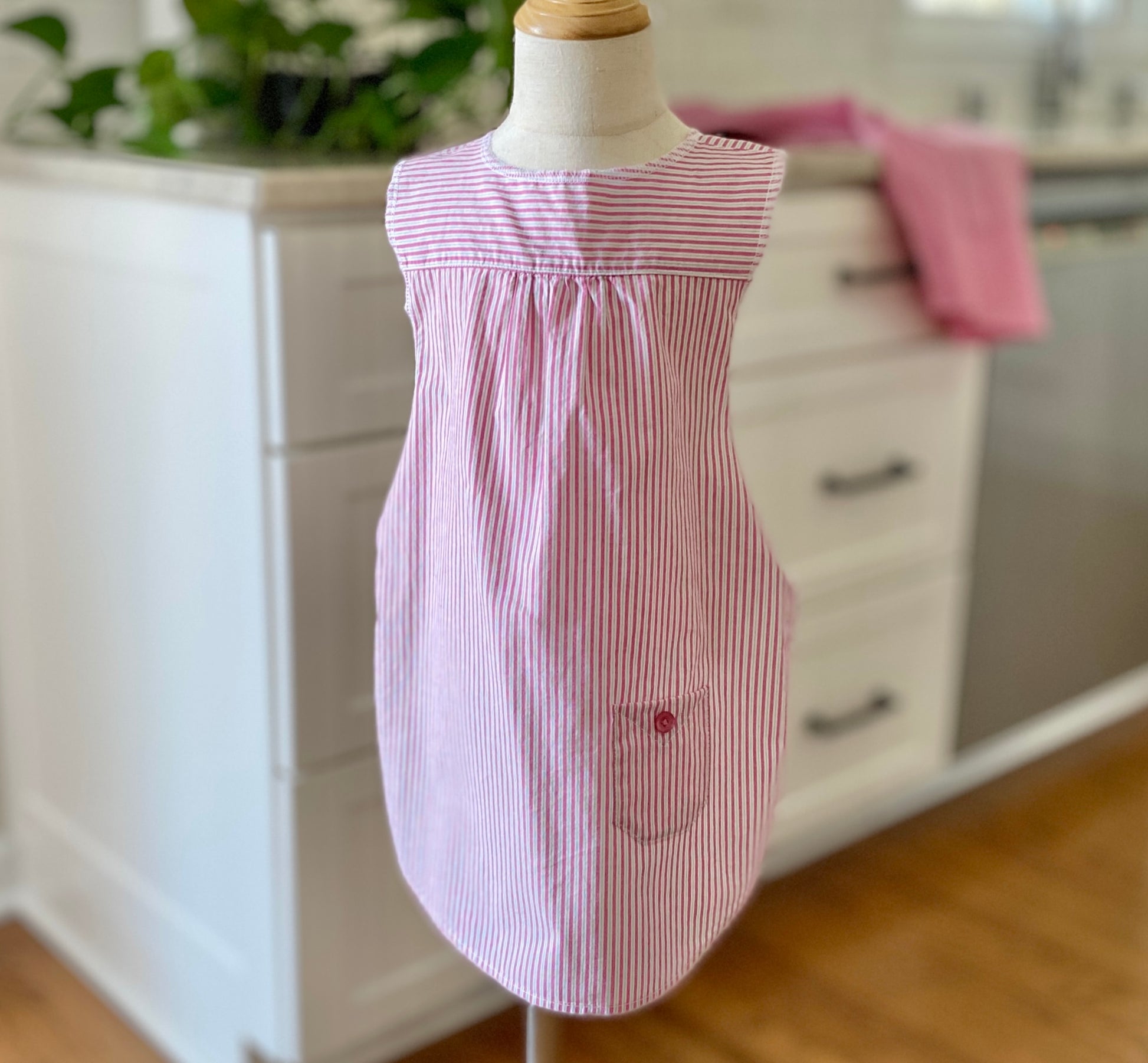 Child mannequin wearing a pink and white striped apron in a kitchen setting