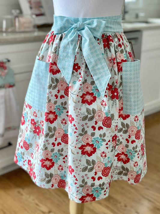 Floral apron with a blue ribbon on a mannequin in a kitchen setting